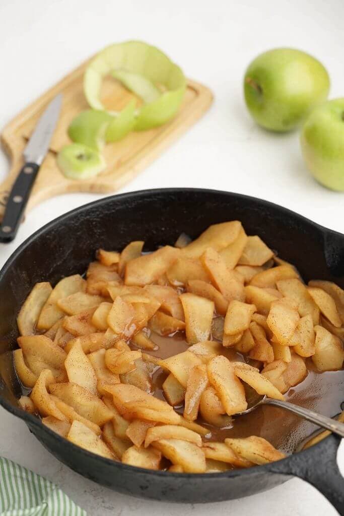Fried apples in cast iron skillet with green apples in the background.