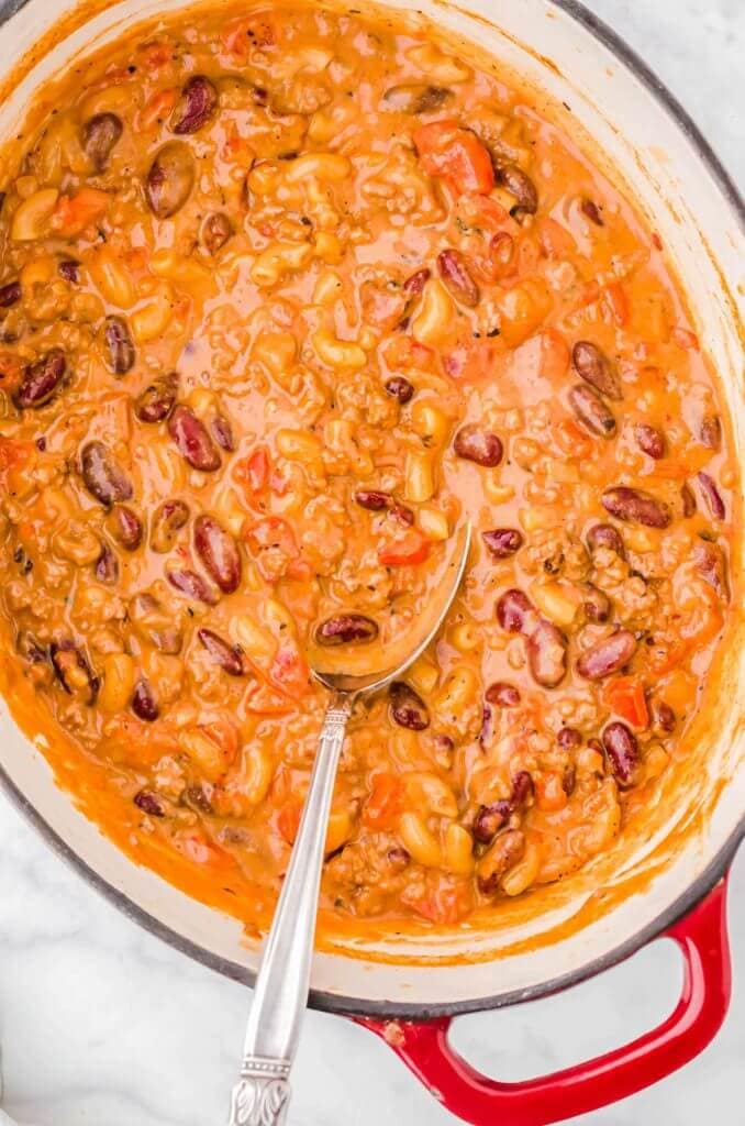 Dutch Oven filled with cheesy chili Mac with serving spoon.