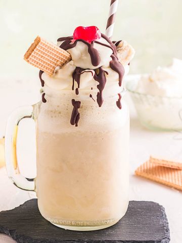 Banana Milkshake with drizzled chocolate, whipped cream and wafers, topped with a cherry.
