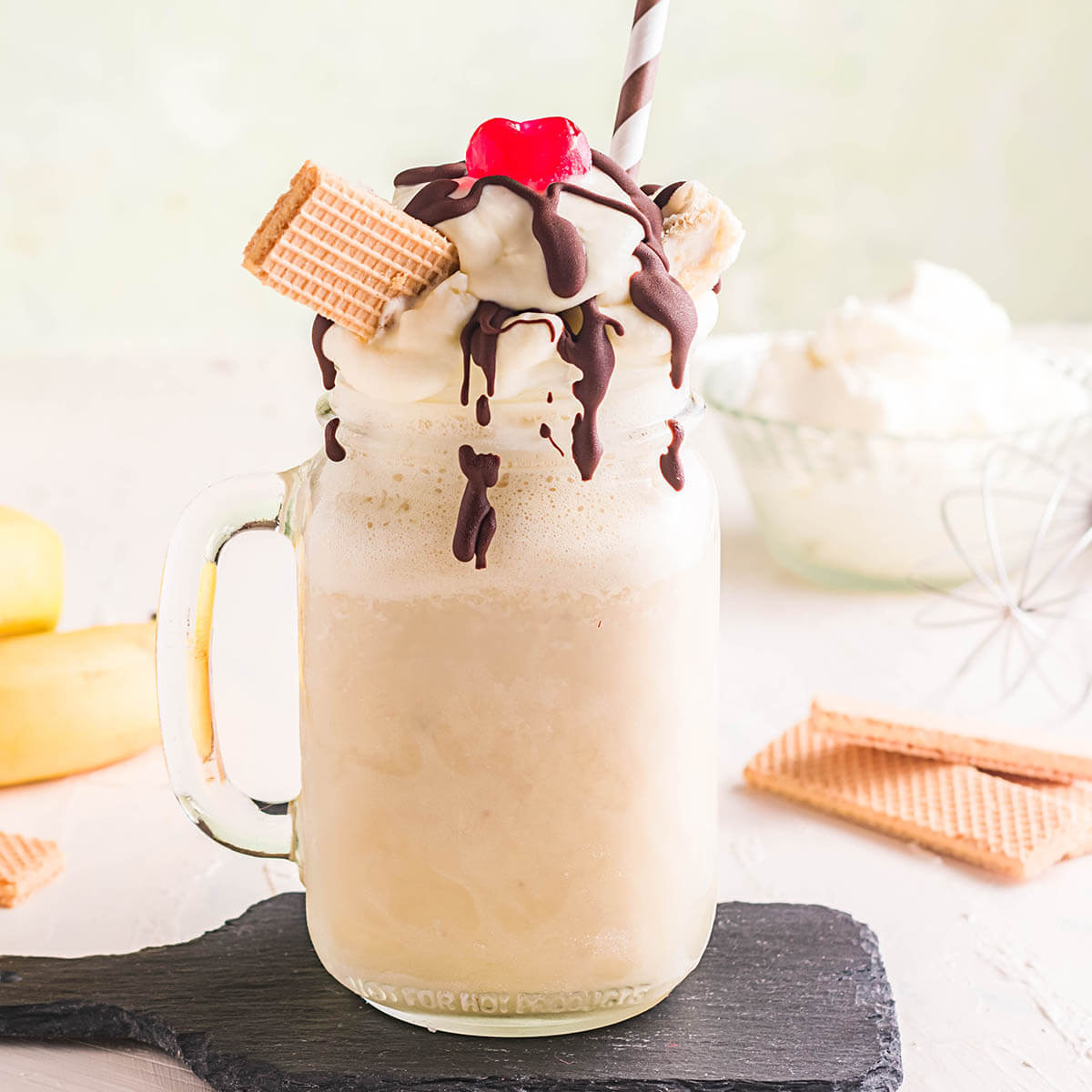 Banana Milkshake with drizzled chocolate, whipped cream and wafers, topped with a cherry.