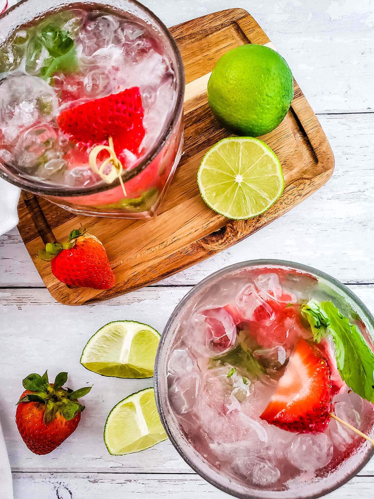 Overhead shot of two cocktail garnished with strawberries and lime.