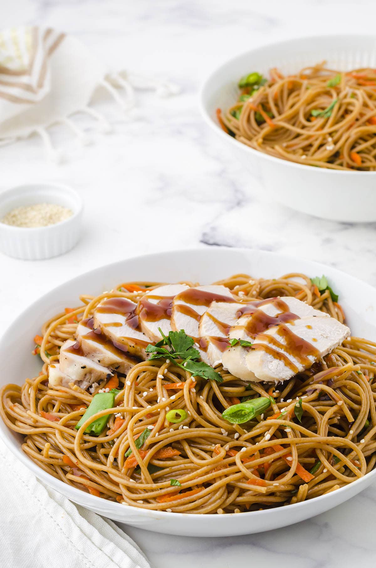 Udon noodles in bowl topped with sliced chicken drizzled with teriyaki sauce.