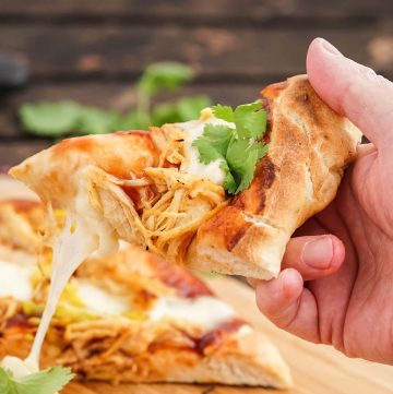Hand holding a slice of bbq chicken pizza.