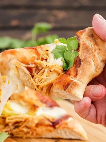 Hand holding a slice of bbq chicken pizza.