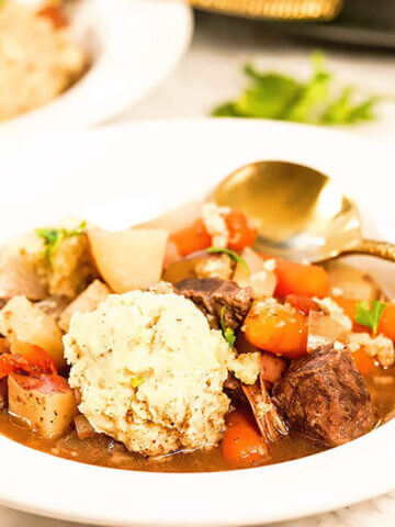 Beef stew with dumplings in white bowl with spoon.