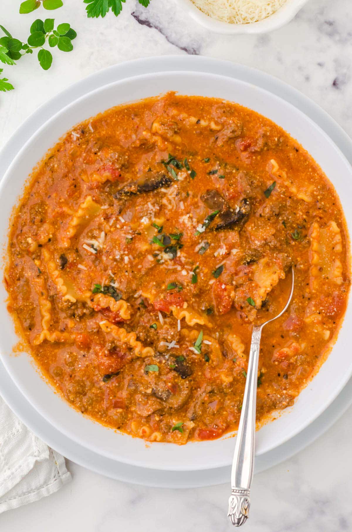 Lasagna soup in white bowl with serving spoon.