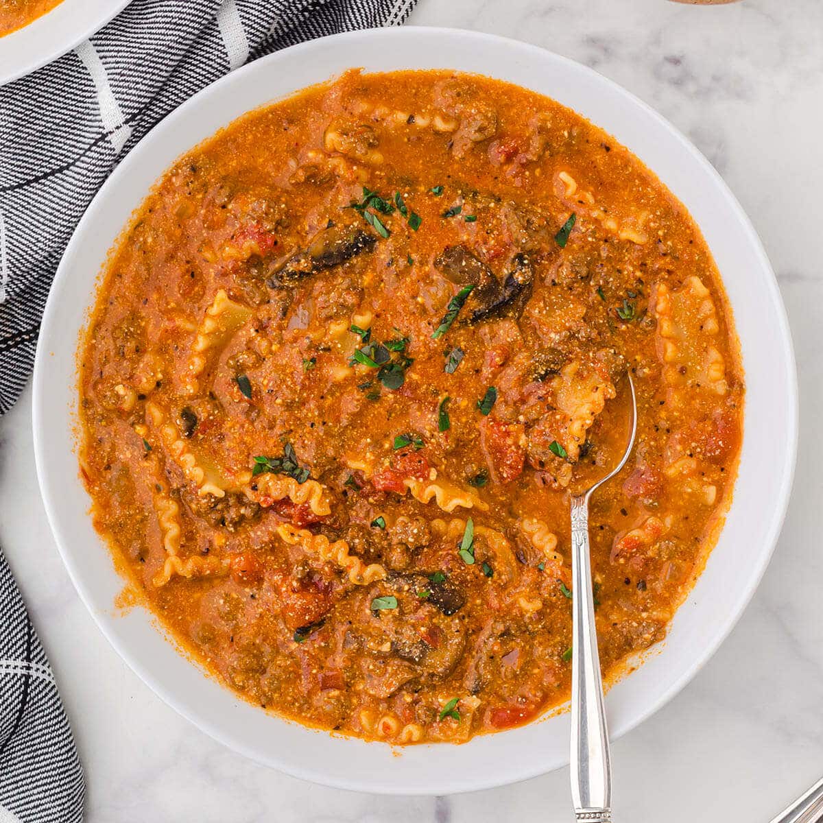 White bowl filled with lasagna soup with serving spoon.