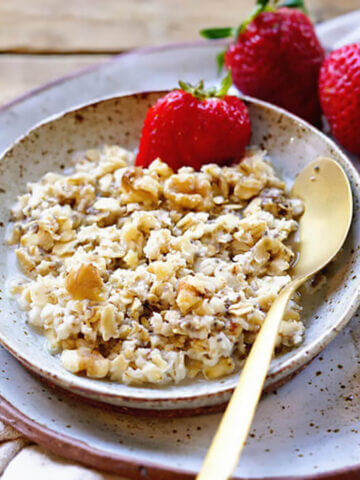 Oatmeal in bowl with spoon, served with strawberries.