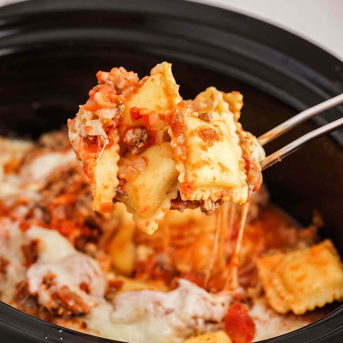 Spooning out a large serving of crockpot ravioli out of slow cooker. 