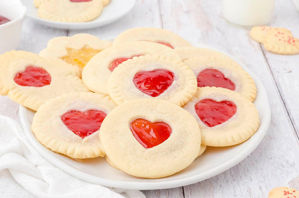 Strawberry Sandwich Cookies on white platter. With heart cutouts that are filled with jam. 