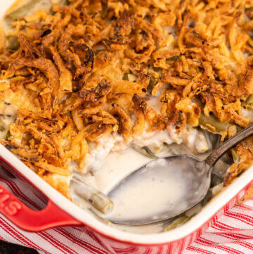 Green bean casserole in baking dish topped with fried onions. With serving spoon.