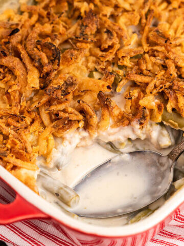 Green bean casserole in baking dish topped with fried onions. With serving spoon.