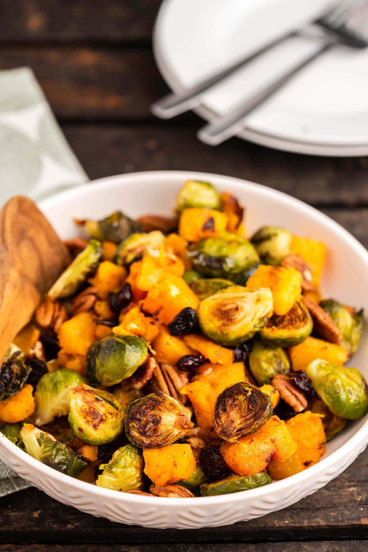 Cooked brussels sprouts and butternut squash in serving bowl with plates and forks in the background. 
