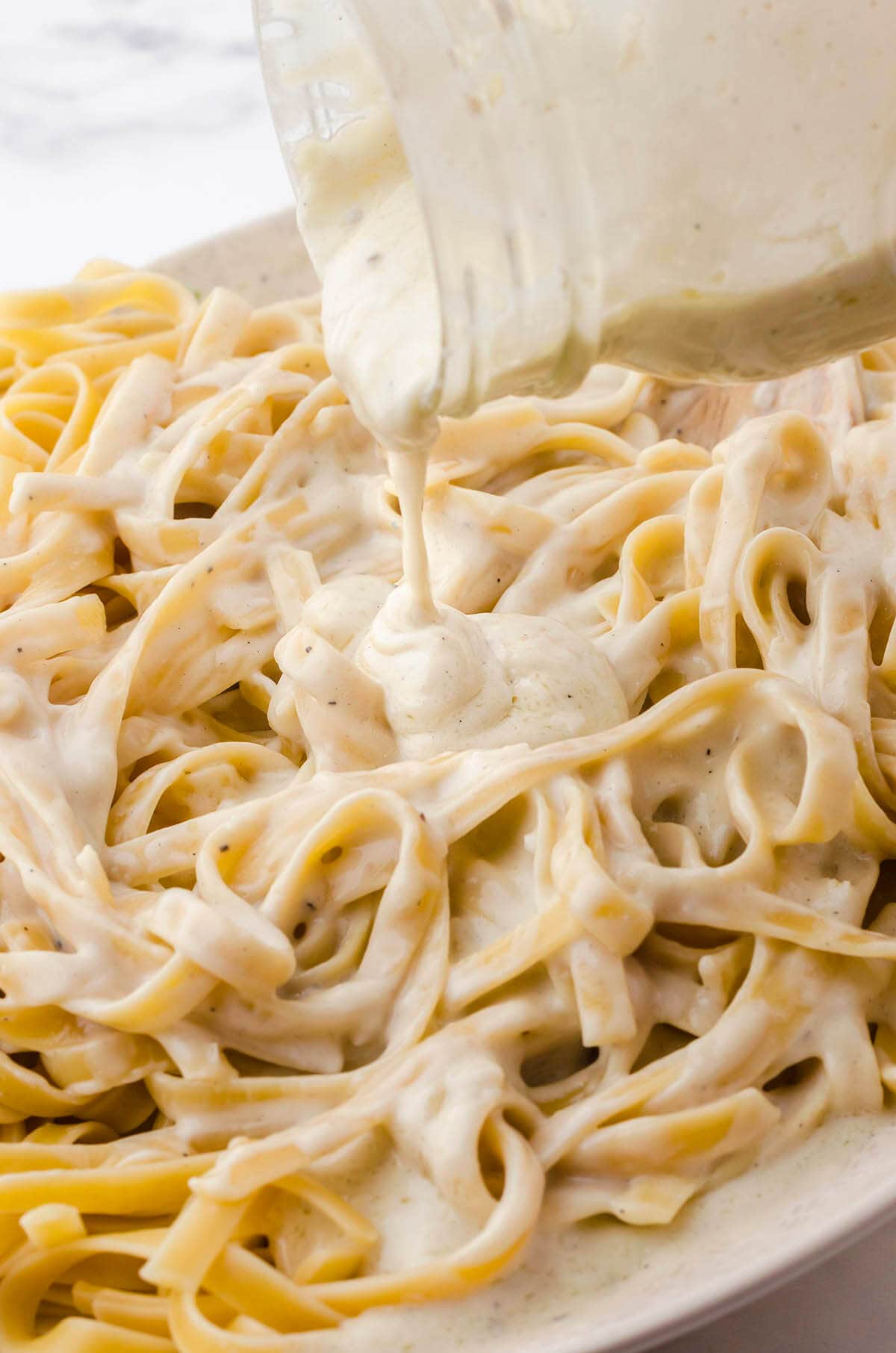 Platter of fettuccini pasta with Alfredo Sauce being poured over it.