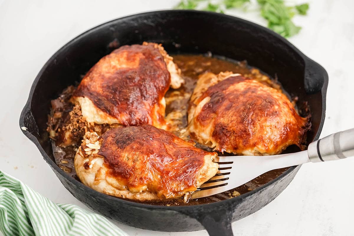 Baked French Onion Chicken in skillet, with serving spoon and garnished with parsley.