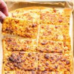 Sliced cheesy breadsticks on baking sheet with hand grabbing a serving.