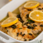 Baked chicken in casserole dish topped with sliced lemon.
