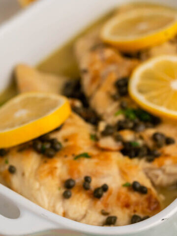 Baked chicken in casserole dish topped with sliced lemon.