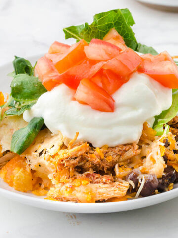 Taco Casserole on plate topped with sour cream, lettuce and diced tomatoes.