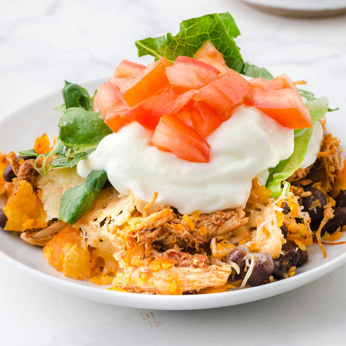 Taco Casserole on plate topped with sour cream, lettuce and diced tomatoes.