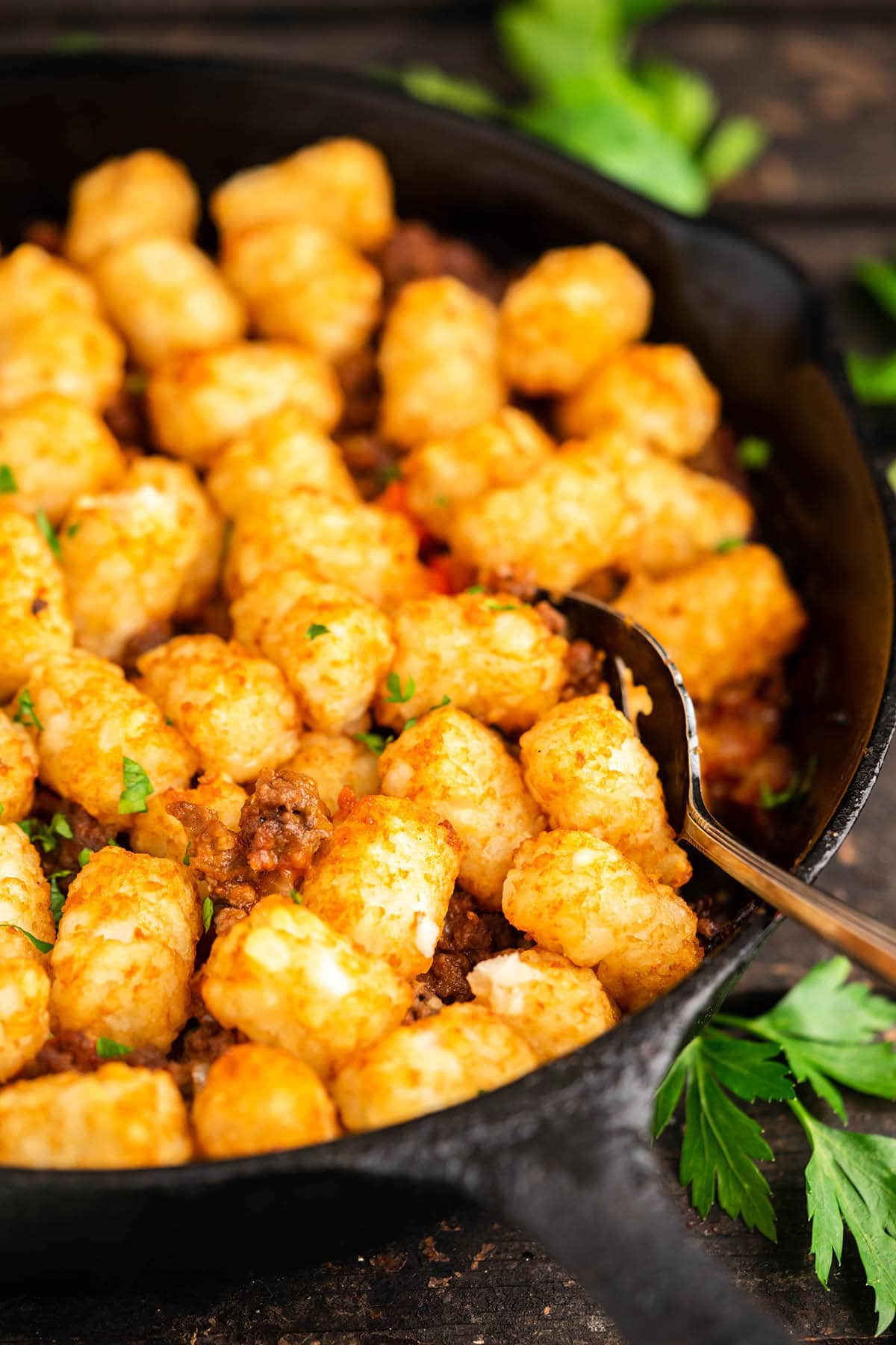 Sloppy Joe Tater Tot Casserole in cast iron skillet, with serving spoon. 