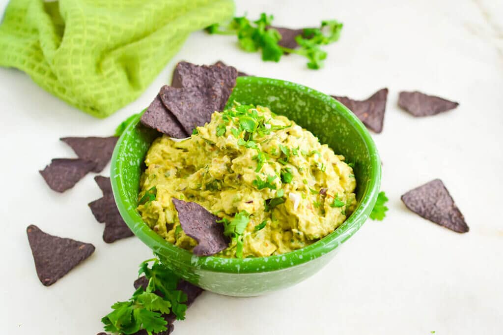 Creamy Guacamole in bowl served with chips.