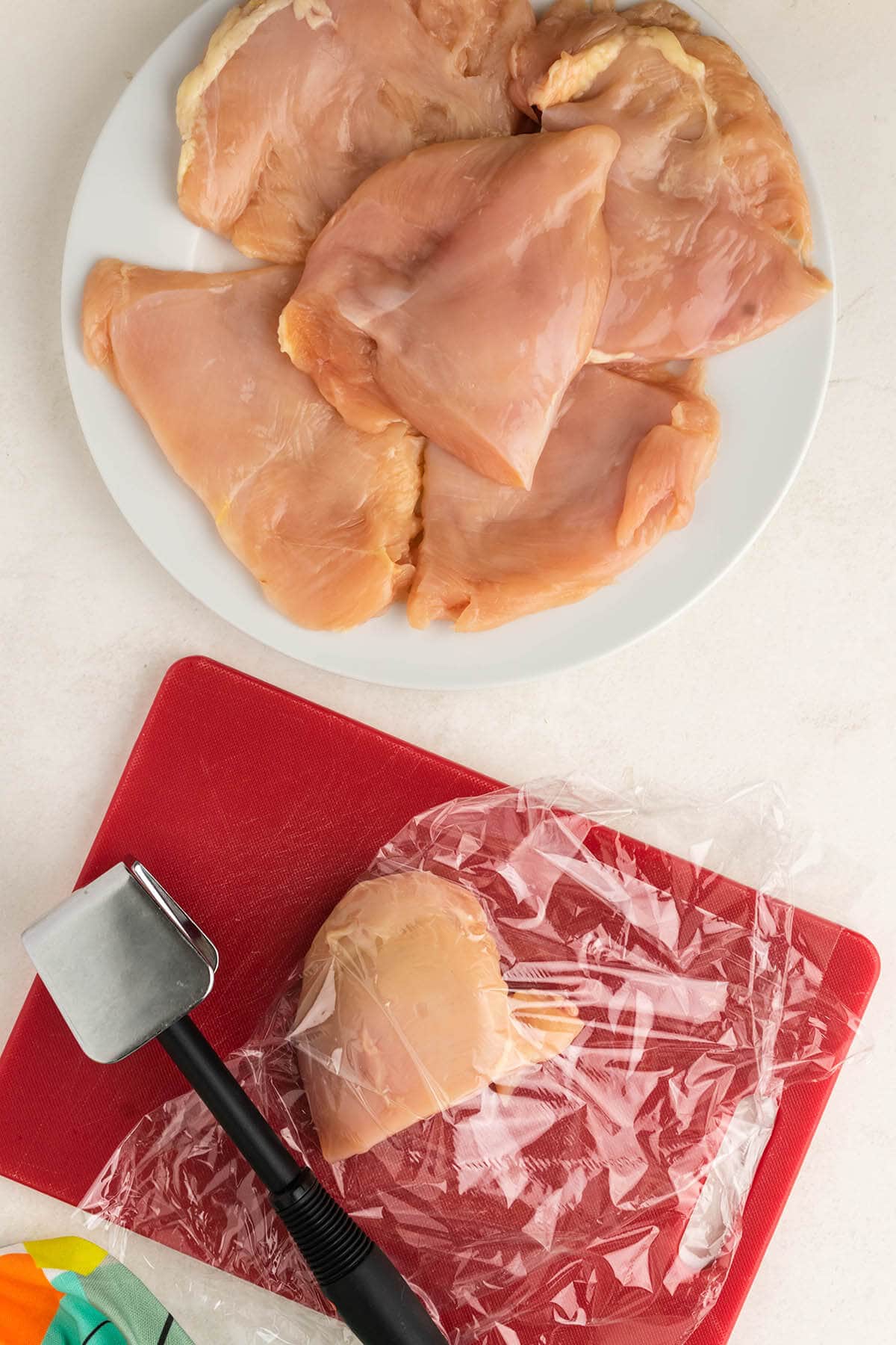 Chicken breast between plastic wrap with meat hammer.