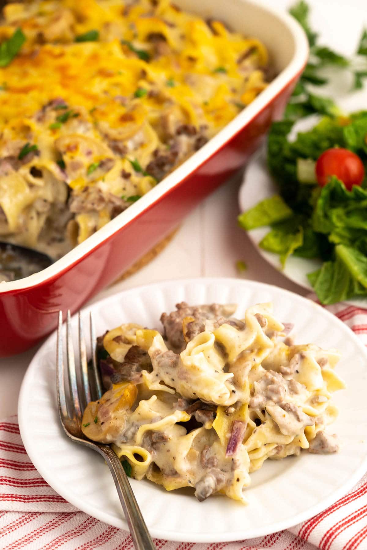 Plate filed with hamburger noodle casserole dish baking dish and salad.