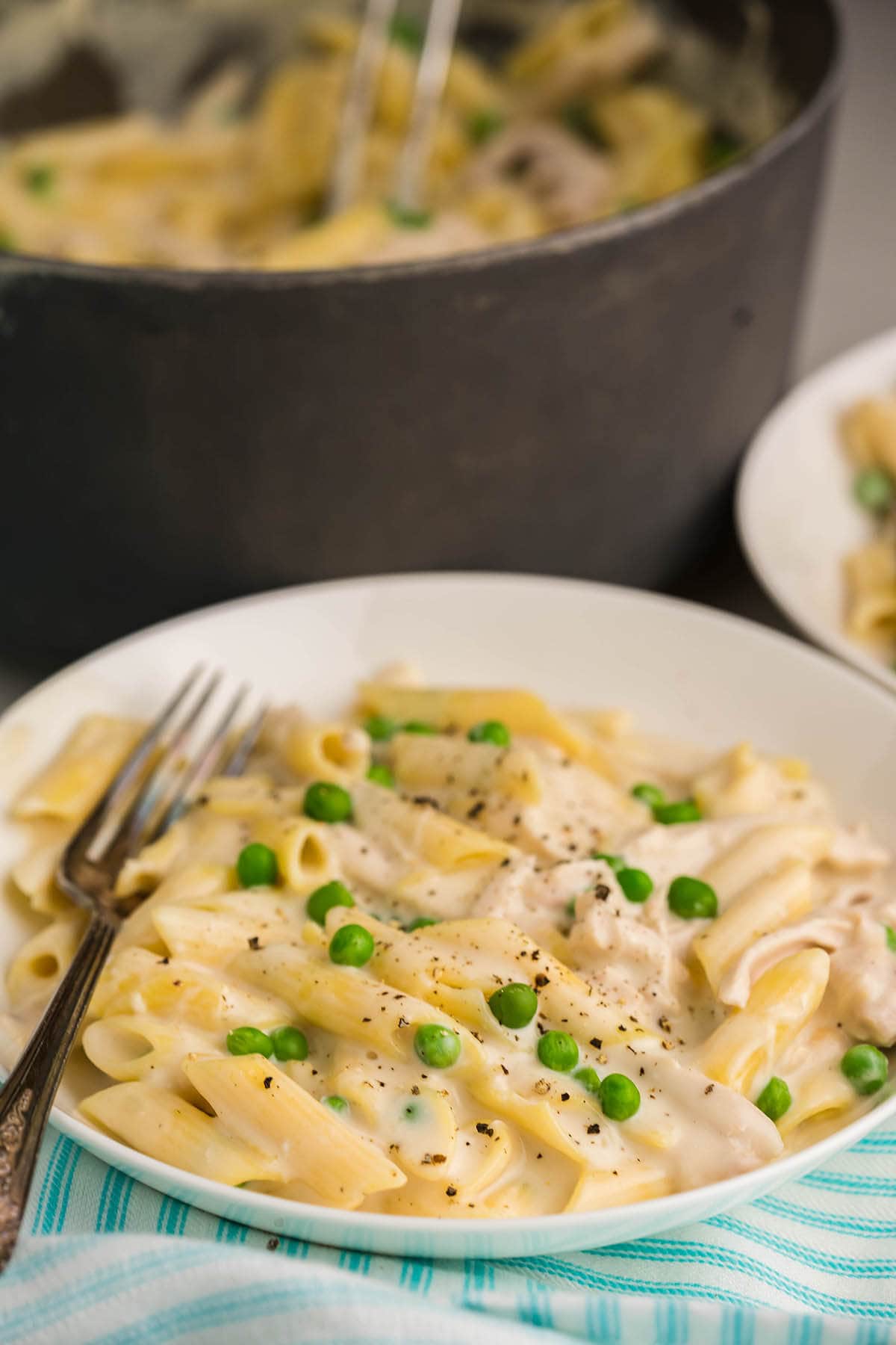 Alfredo Chicken with peas in bowl with fork. With Dutch Oven filled with pasta in the background. 