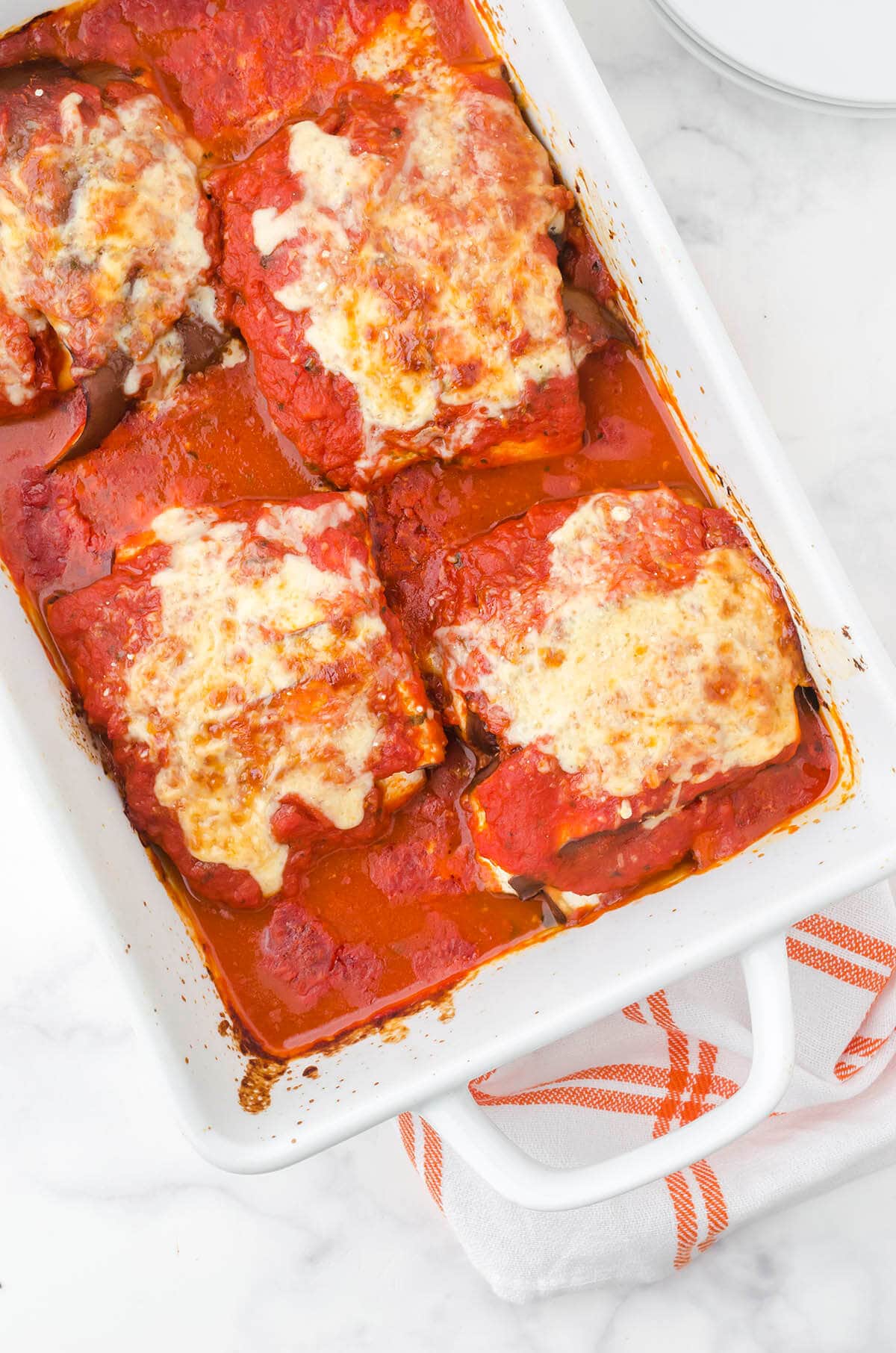 Eggplant rollups in casserole dish topped with sauce and cheese.