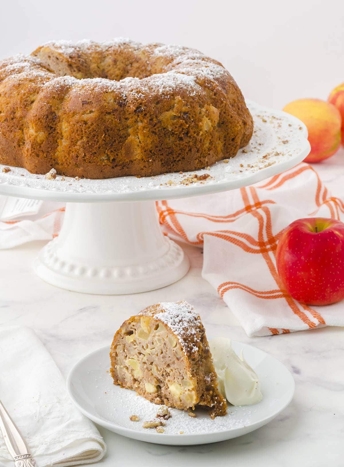 Apple Bundt Cake on cake stand with slice of cake on serving plate.