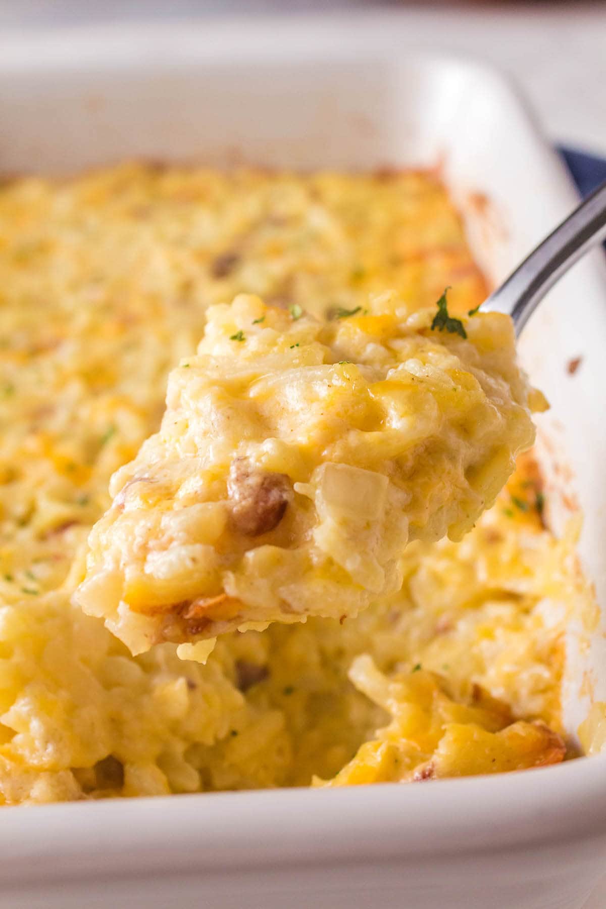 Cheesy potatoes in casserole dish with serving spoon.