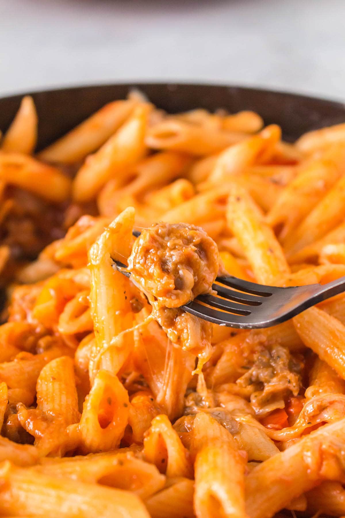 Saucy penne pasta in dish with fork filled with pasta. 