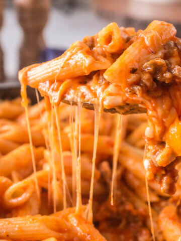 Cheesy pasta in casserole dish with spoon dishing up a helping.