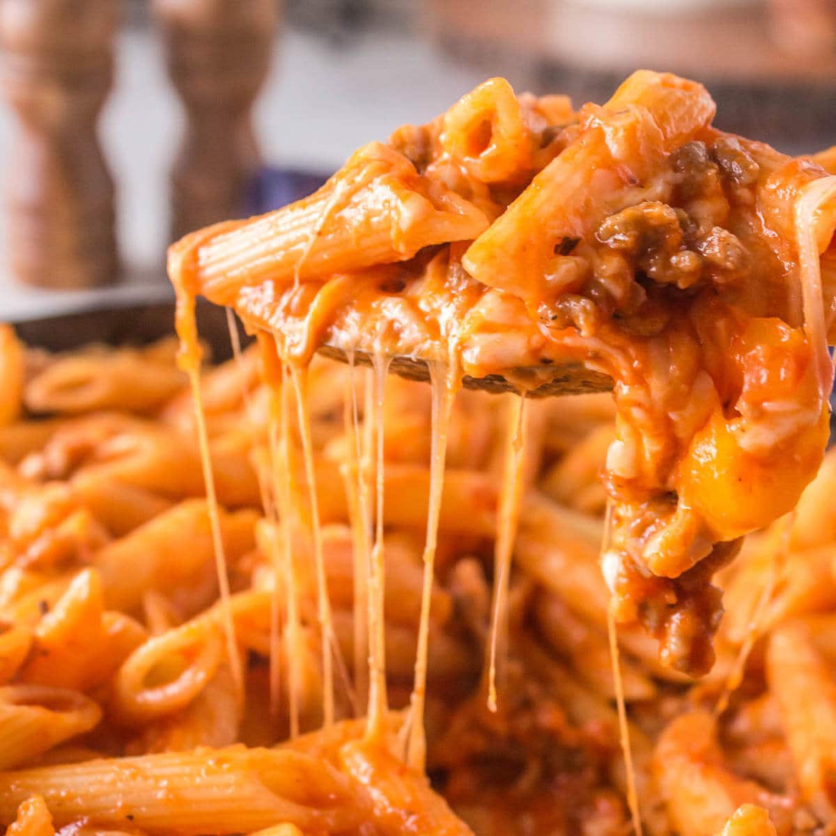 Cheesy pasta in casserole dish with spoon dishing up a helping.