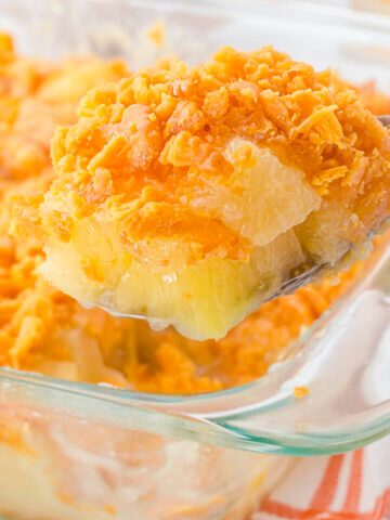 Pineapple Casserole in baking dish with serving spoon taking big scoop.