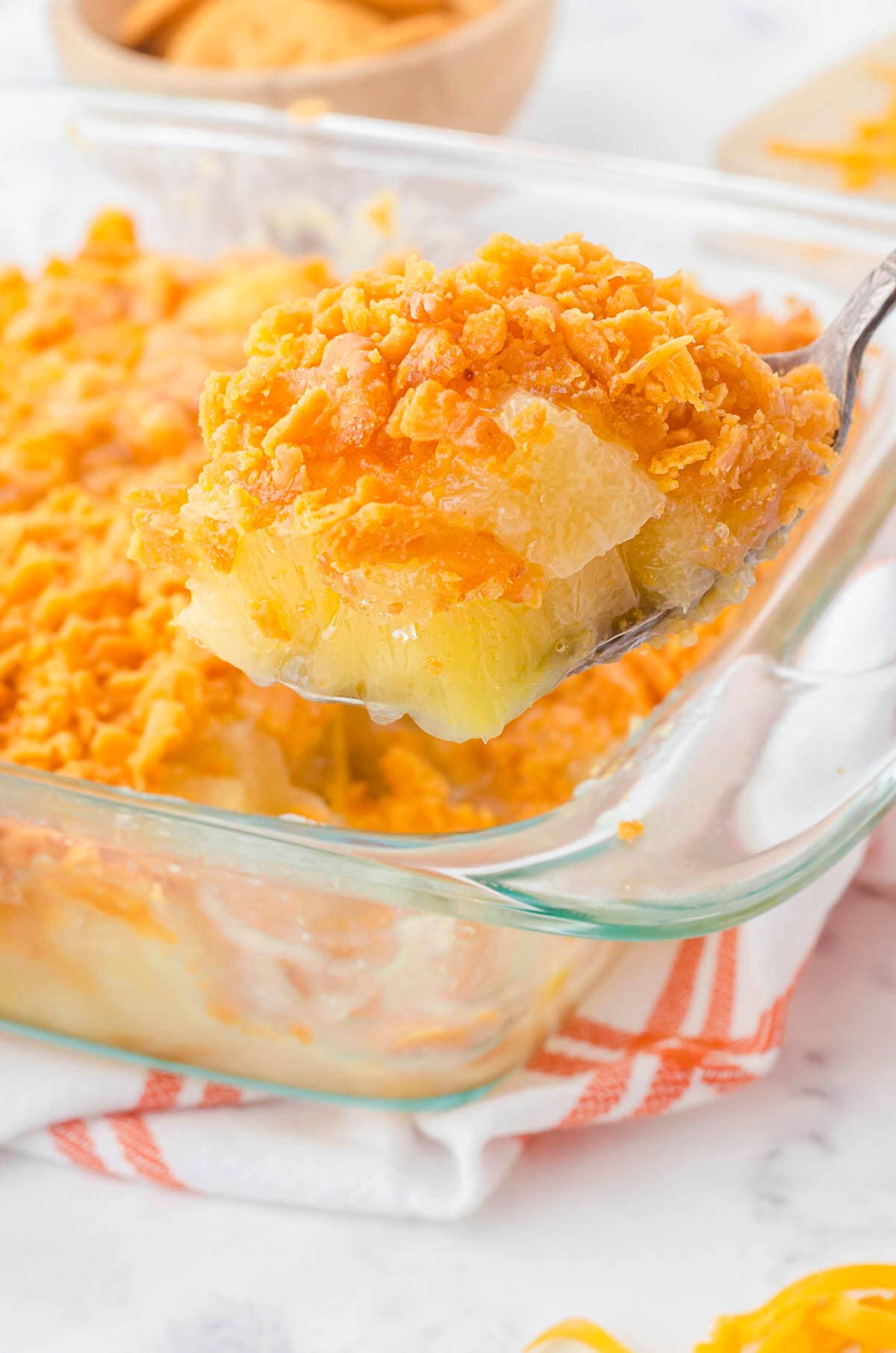 A spoon holding a serving of cheesy pineapple casserole. 