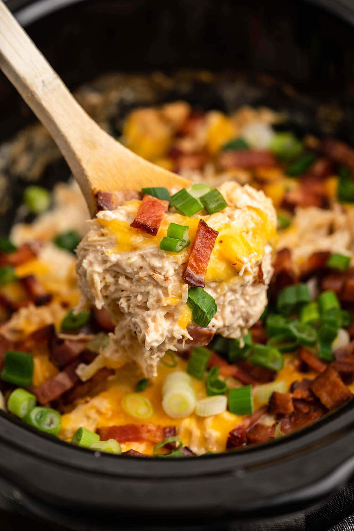 Crack Chicken in slow cooker with wooden serving spoon.