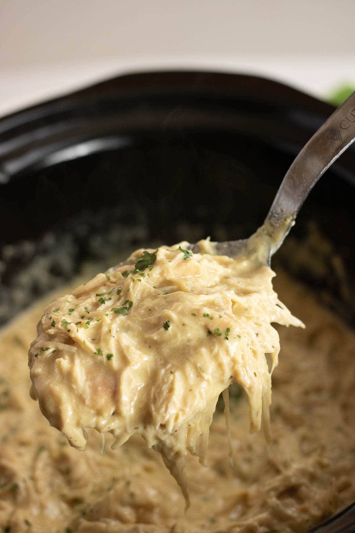 Juicy shredded ranch chicken in slow cooker with serving spoon.