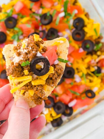 Loaded tortilla chip with ground beef taco dip recipe in the foreground.