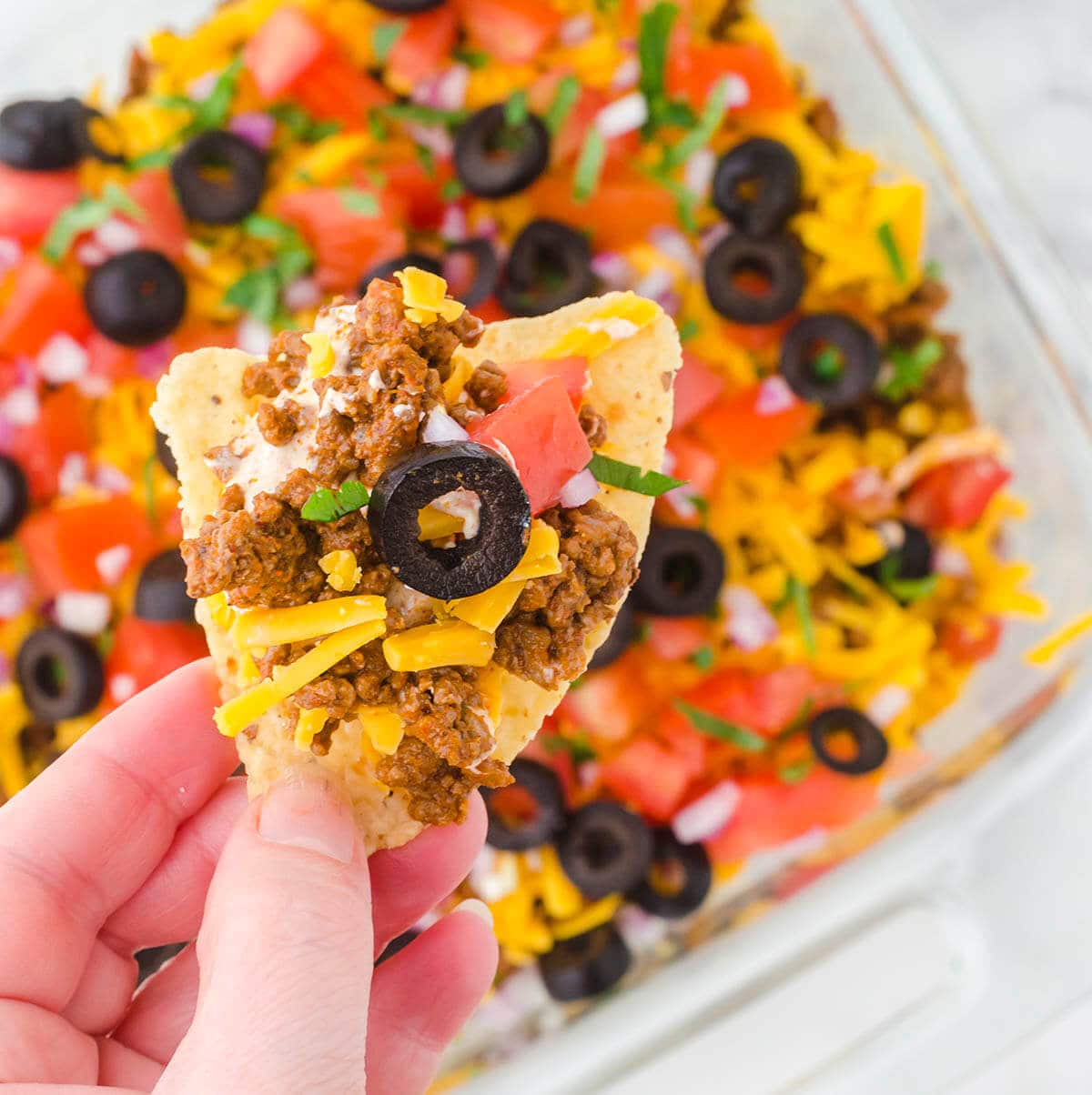 Loaded tortilla chip with ground beef taco dip recipe in the foreground.