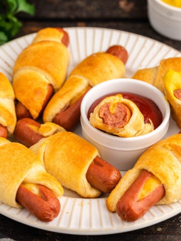 Pigs in a blanket on platter with ketchup and mustard.