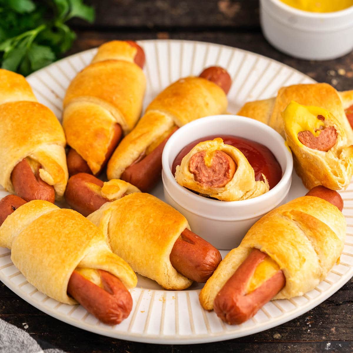 Pigs in a blanket on platter with ketchup and mustard.
