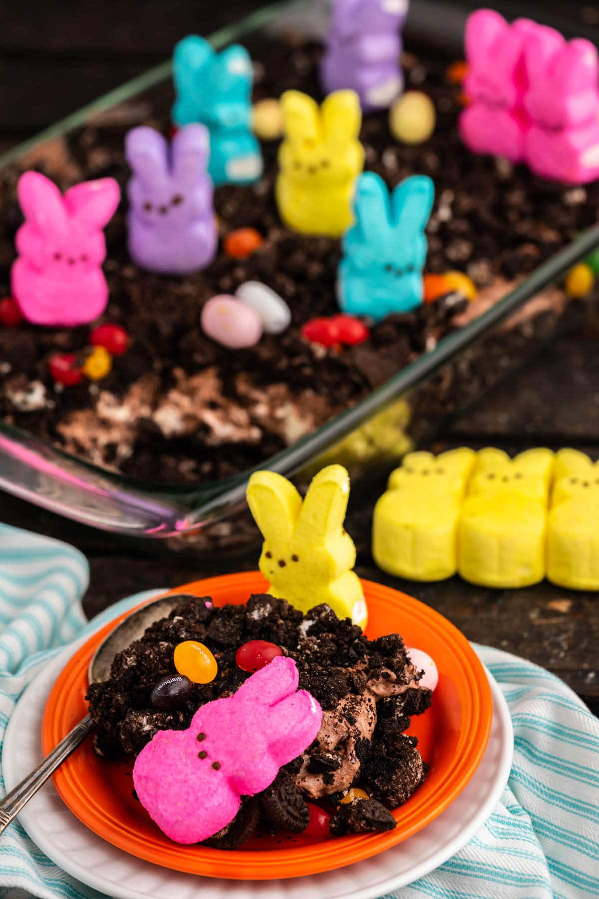Chocolate cake decorated with peeps and candy Easter eggs, with serving on plate. 