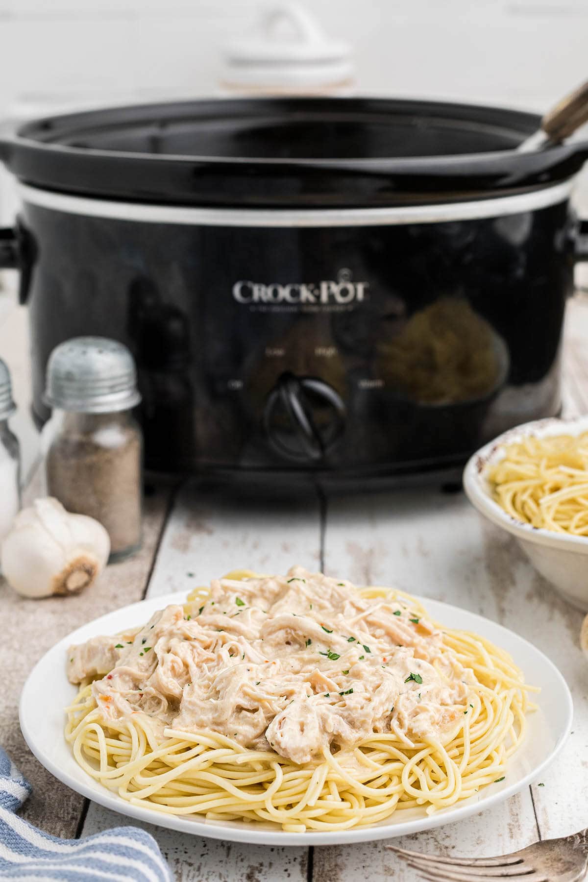 Crockpot Angel Chicken on plate over spaghetti with crockpot.