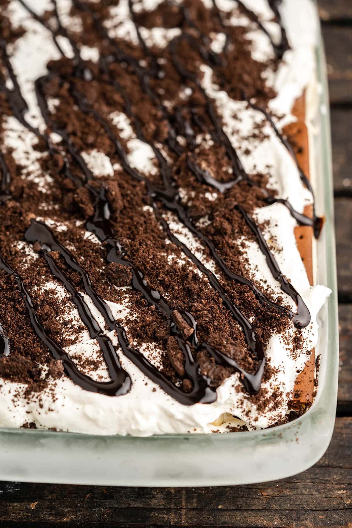 Ice Cream Cake topped with crushed Oreo cookies and drizzled with chocolate sauce in baking dish. 