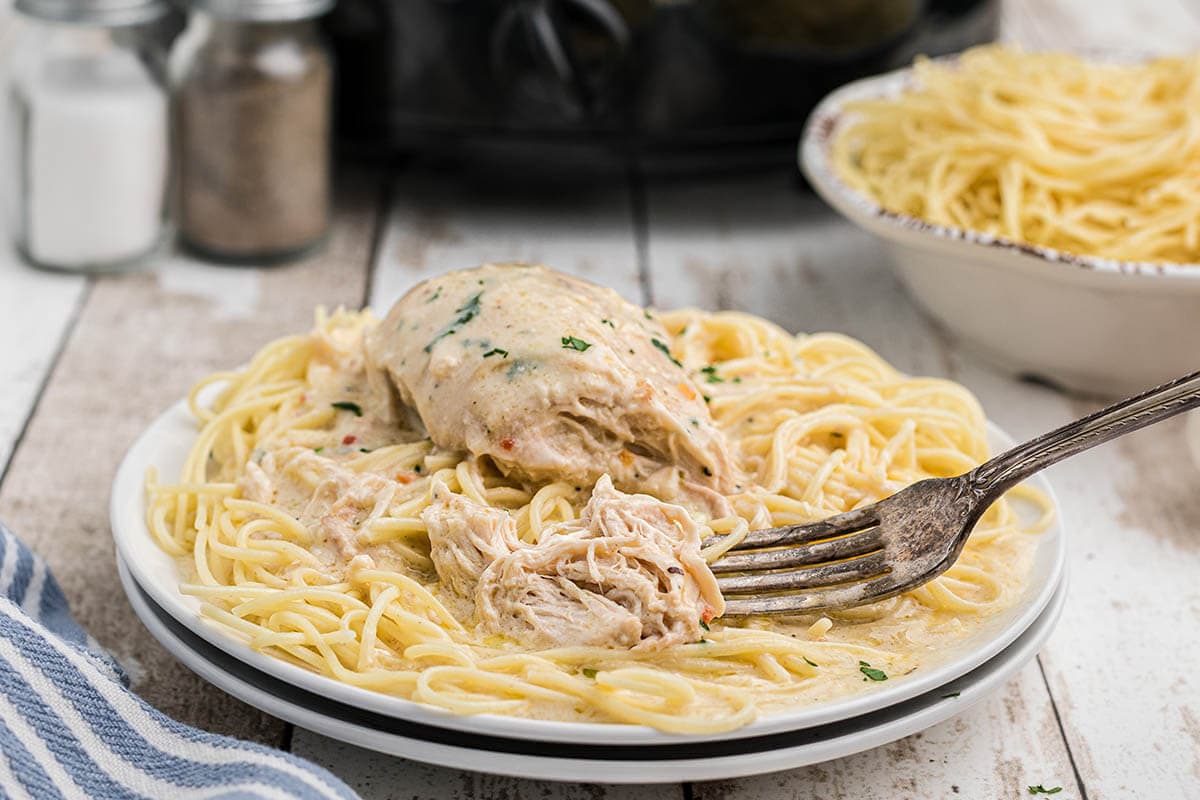 Chicken breast and sauce over spaghetti noodles with fork.