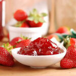 Strawberry Freezer Jam in bowl surrounded by fresh strawberries.