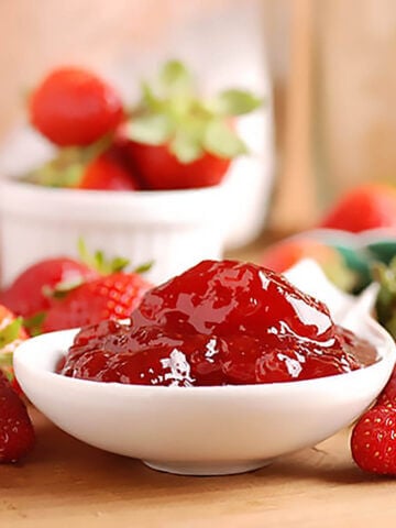 Strawberry Freezer Jam in bowl surrounded by fresh strawberries.