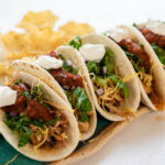 Chicken soft tacos topped with shredded lettuce, salsa and sour cream.